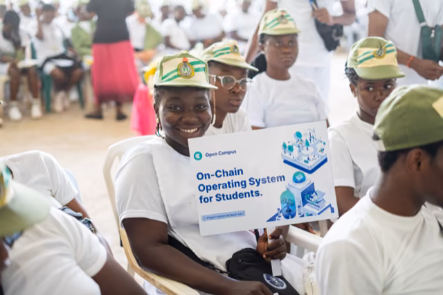A smiling corps member holds an Open Campus board