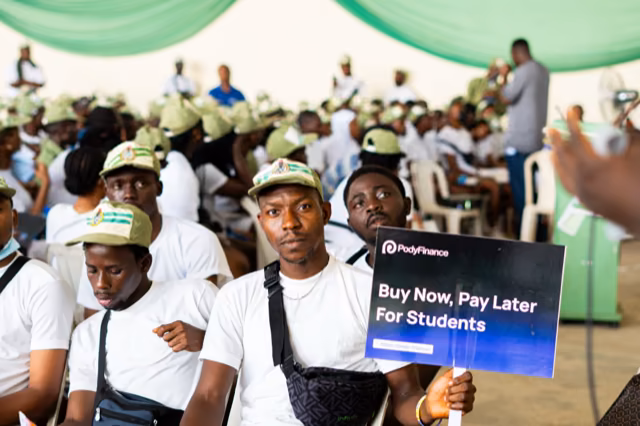 A corps member holds a Pody Buy Now, Pay Later for Students board